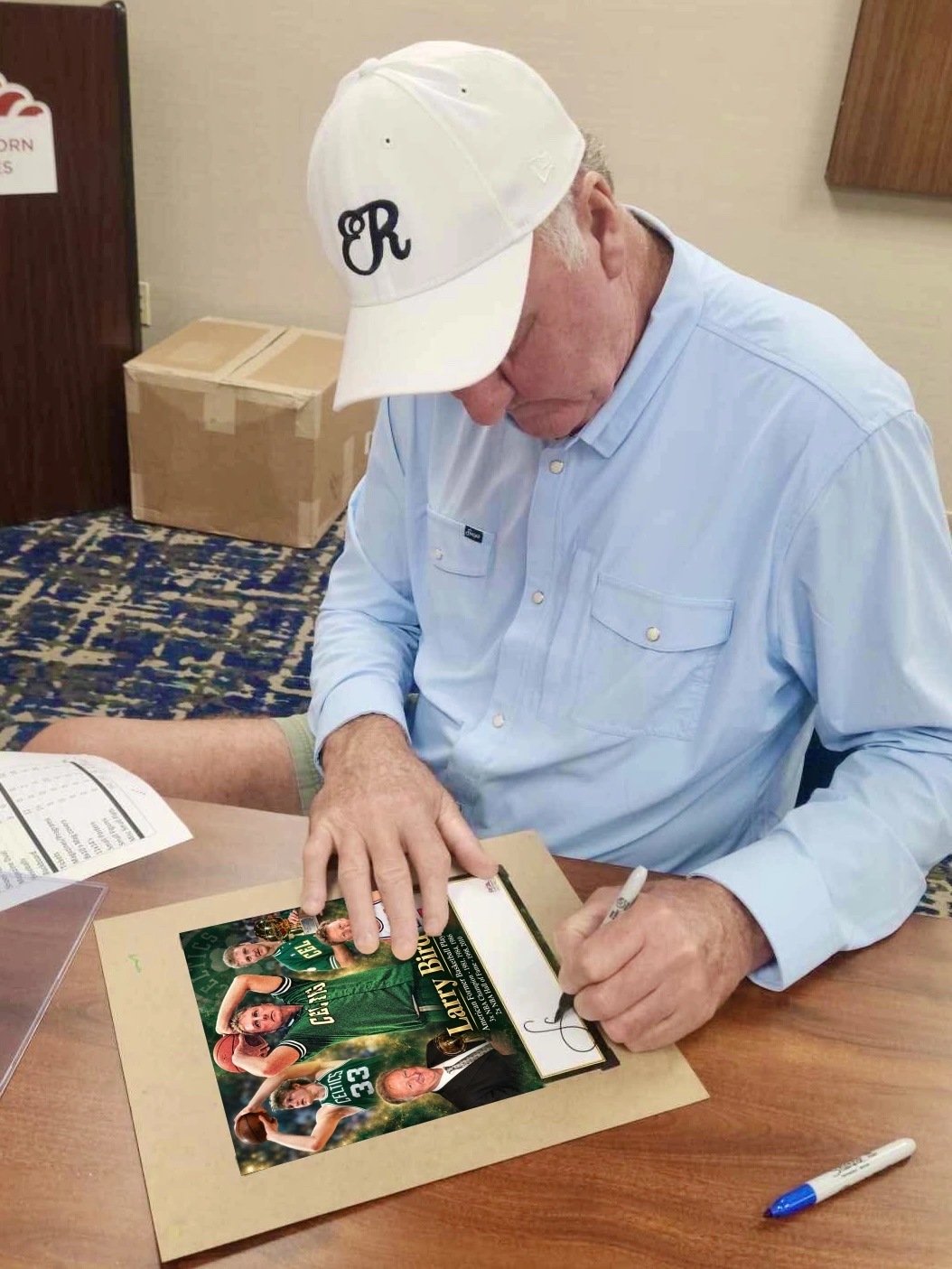 Larry Bird at the signing table with a custom collage.